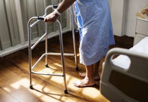 Person holding a walking frame as they crouch in pain in a hospital gown